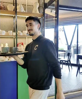Un garzón lleva una bandeja con tazas frente a las repisas de yesos