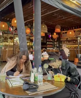 Dos amigas pintan en una mesa redonda bajo lámparas de mimbre