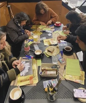 Un grupo pinta tarjetas y figuras en una mesa larga del café